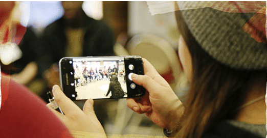 Un étudiant utilise un smartphone pour enregistrer ou prendre une photo d'un groupe de personnes. La scène est capturée sur l'écran du téléphone.